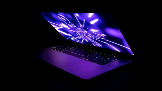 Aufgeklappter Laptop mit violett leuchtendem Bildschirm im dunklen Raum – Sexchat sicher nutzen