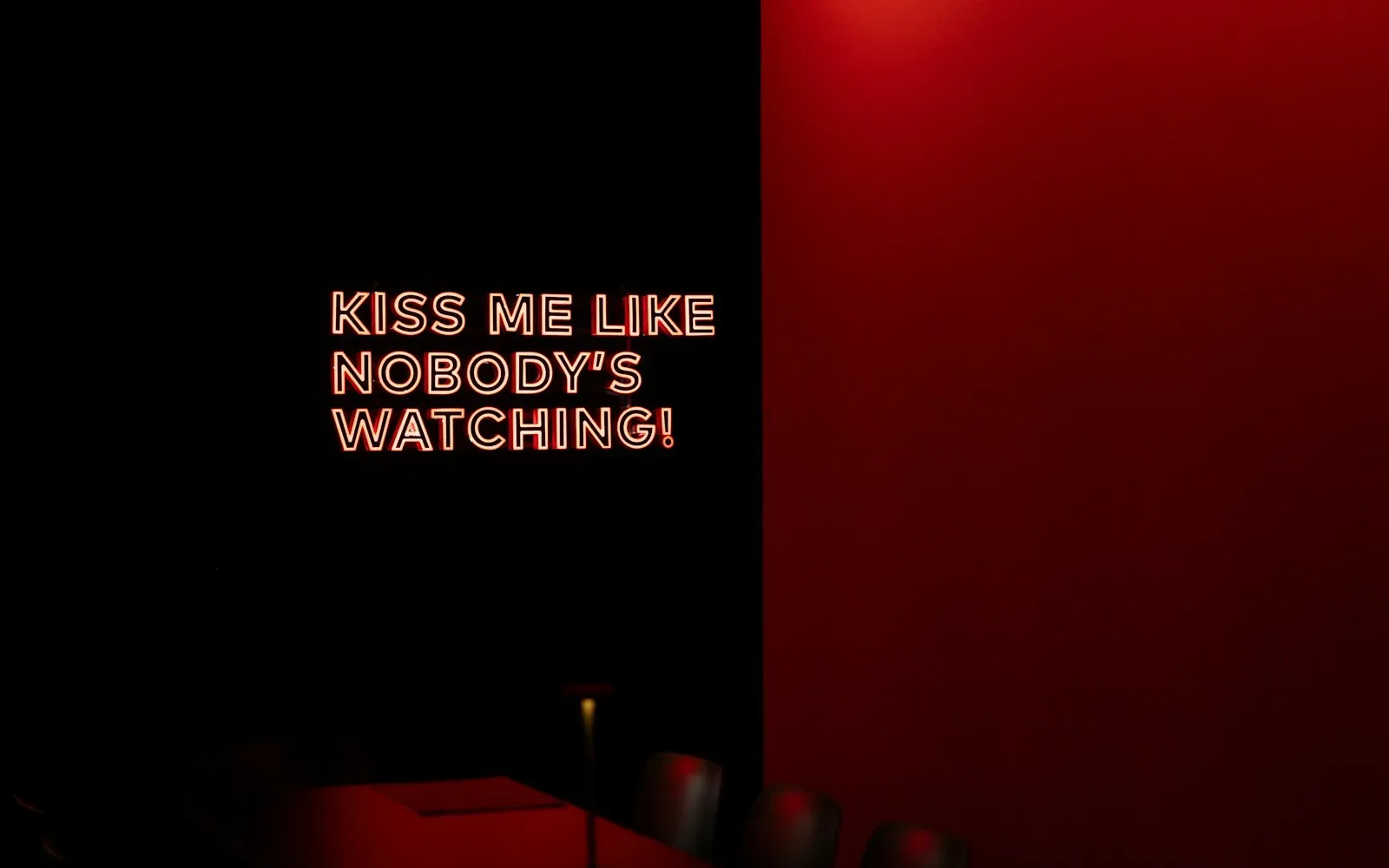 Roter Neon-Schriftzug „Kiss me like nobody’s watching“ an einer dunklen Wand – kostenloser Sexchat ohne Anmeldung