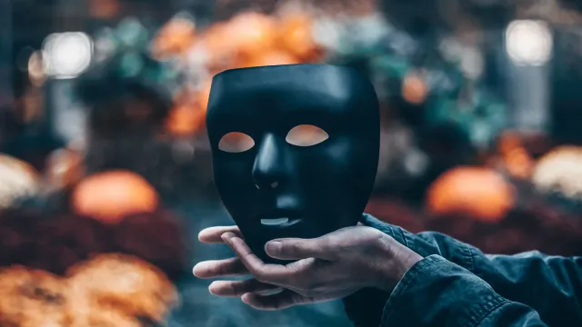 Hand hält eine schwarze Maske vor unscharfem Hintergrund – Sexchat Nickname Ideen
