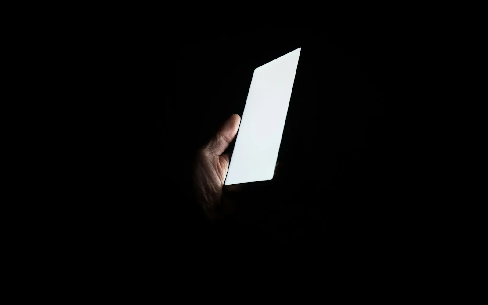 Hand hält ein hell leuchtendes Smartphone im völlig dunklen Raum
